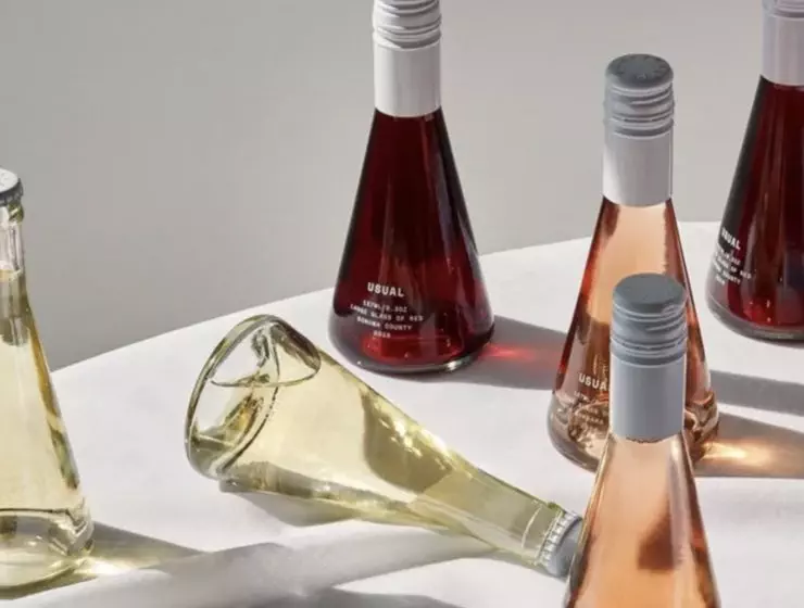 Various bottles of wine are arranged on a surface, with one tipped over, against a neutral background.