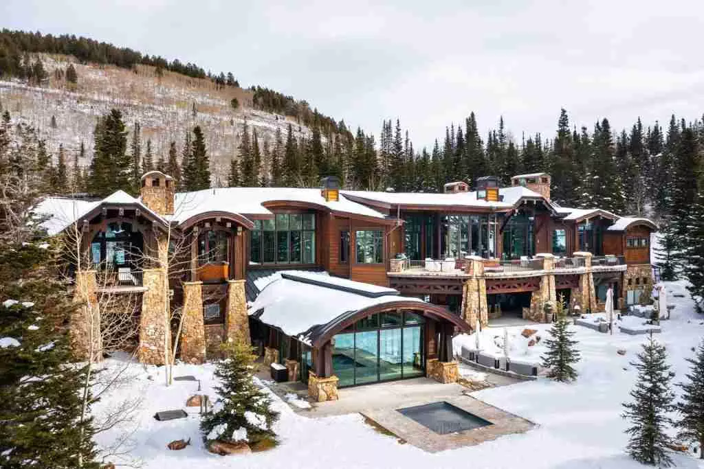 A large cabin-style mountain resort surrounded by snow-covered trees and landscape under a cloudy sky.