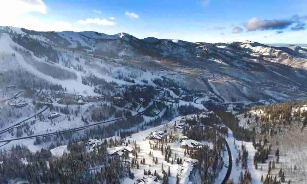 Aerial view of a snow-covered mountainous landscape with winding roads and scattered buildings amidst the trees.